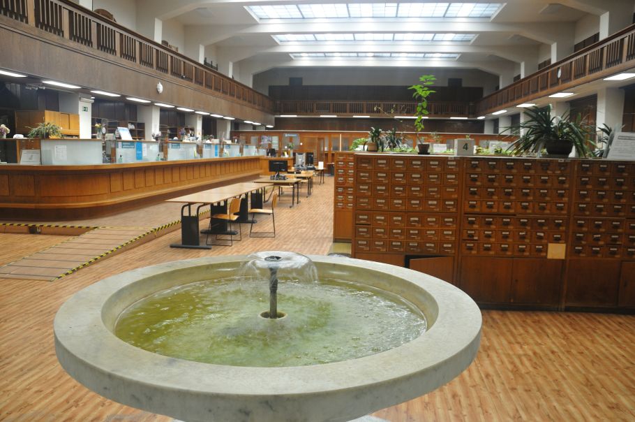 Zdjęcie holu biblioteki, na pierwszym planie okrągła fontanna, za nią widoczne katalogi kartkowe oraz stanowiska obsługi czytelników.
