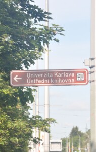 Zdjęcie znaku informacyjnego na latarni miejskiej, strzałka wskazuje kierunek dojścia do Biblioteki Głównej Uniwersytetu Karola.