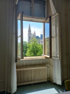 Zdjęcie otwartego okna, za oknem widok na strzelistą wieżę i drzewa.