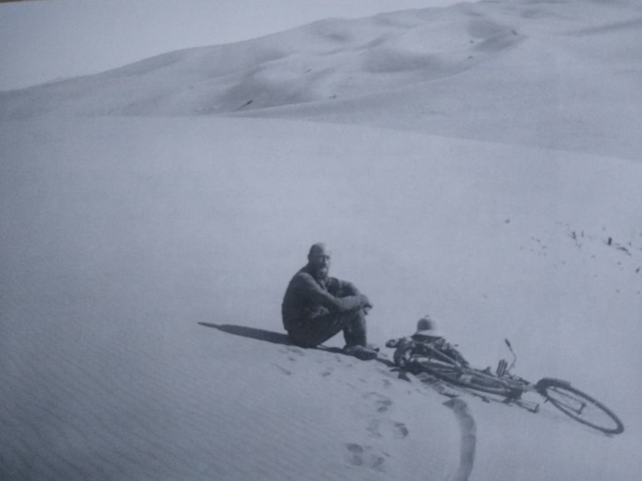 Zdjęcie mężczyzny siedzącego na wydmie, przy nim, leżący rower.