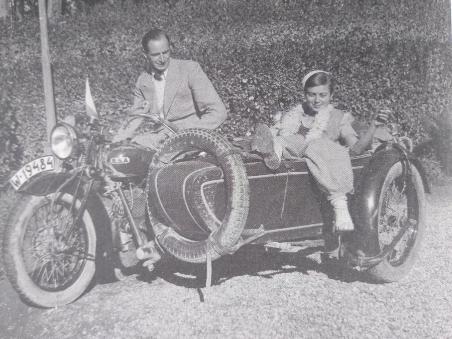 Zdjęcie mężczyzny i kobiety w strojach z lat międzywojennych usadowionych na motorze z doczepionym koszem.