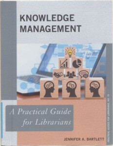 Okładka książki Knowledge Management, na niej ustawione w piramidę drewniane klocki z rysunkami wykresów itp.