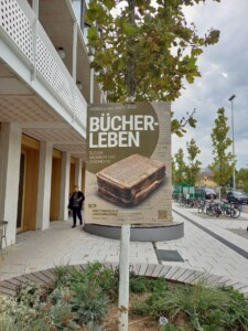 plakat Bücher leben przedstawiający nadpaloną książkę bez okładek, plakat przymocowany do drzewa