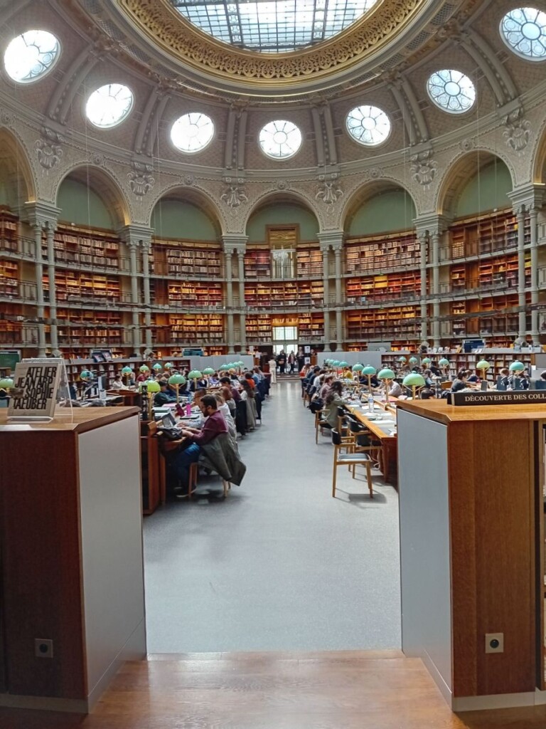 obszerne pomieszczenie z regałami z książkami wzdłuż ścian, zwieńczone ozdobną kopułą, wypełnione czytającymi ludźmi