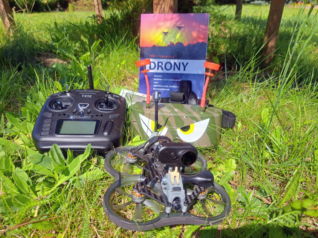 Ułożone na trawie, dron, książka, gogle fpv i radio.