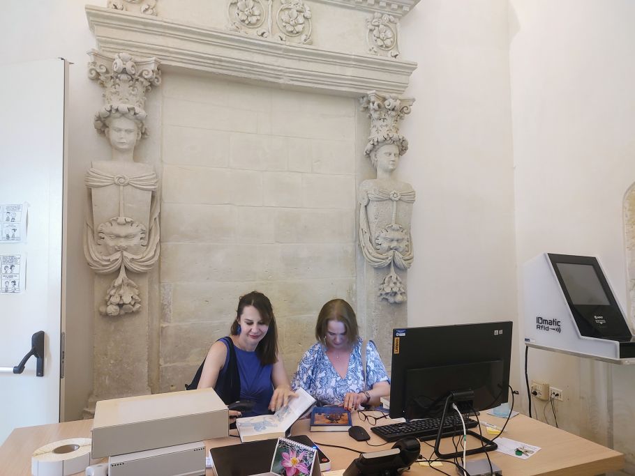 dwie osoby pracują przy komputerze, za nimi ściana z ozdobną płaskorzeźbą