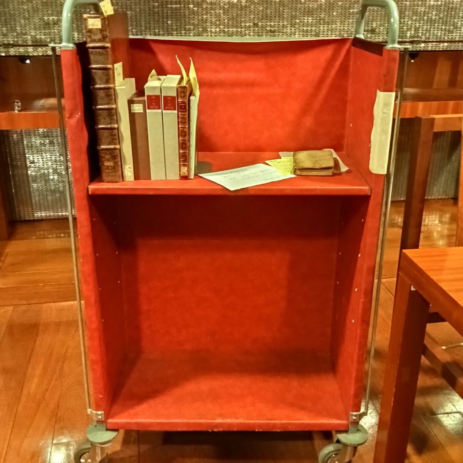 Wózek biblioteczny obity czerwonym atłasem.