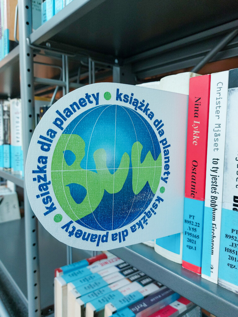 Książki na półce bibliotecznej oznaczone plakietką "Książka dla planety"