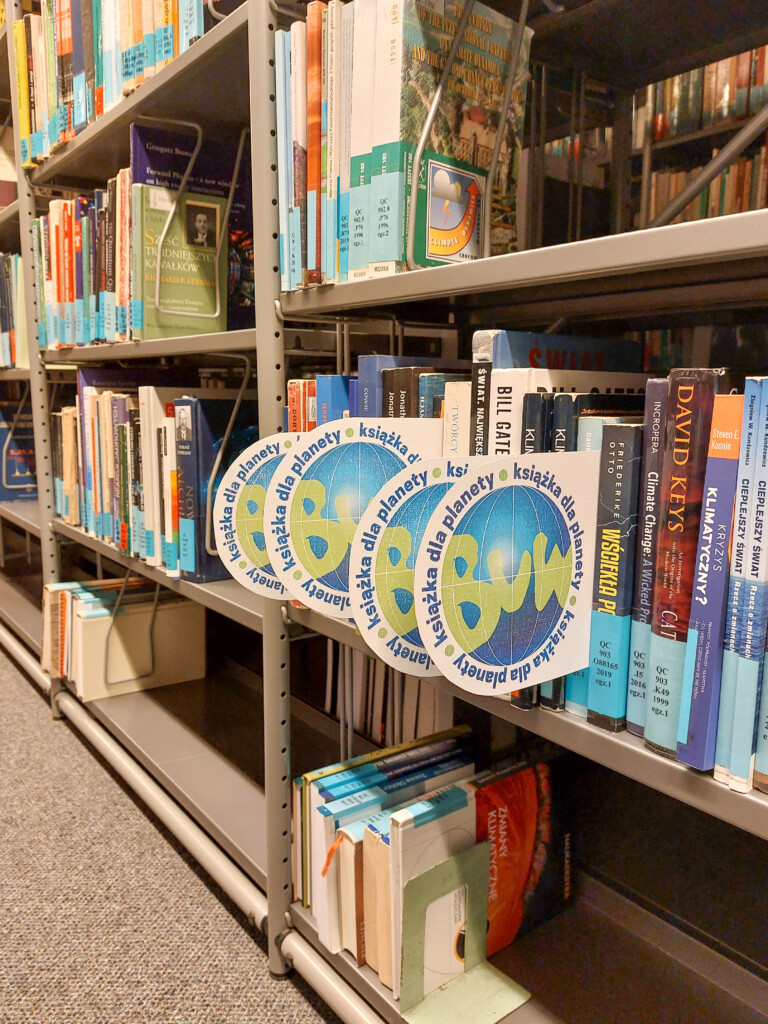 Książki na półce bibliotecznej oznaczone plakietką "Książka dla planety"