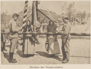 Mężczyźni w mundurach Armii Austro-Węgierskiej kontrolują przy szlabanie dokumenty kobiet w strojach ludowych, zdjęcie czarno-białe