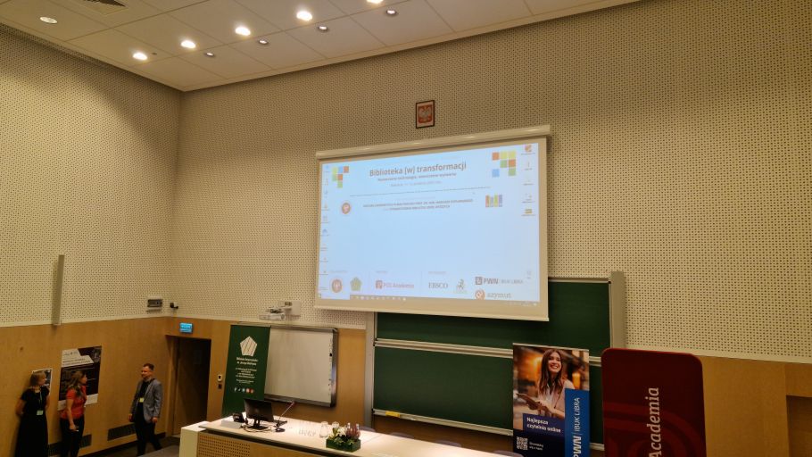 Zdjęcie stali konferencyjnej, na ekranie widoczny tytuł konferencji - Biblioteka w transformacji